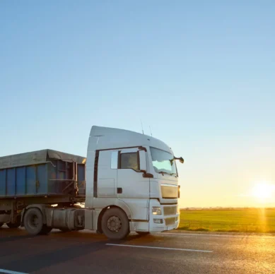 Semi-truck with tipping cargo trailer transporting sand from quarry driving on highway hauling goods in evening. Delivery transportation and logistics concept.